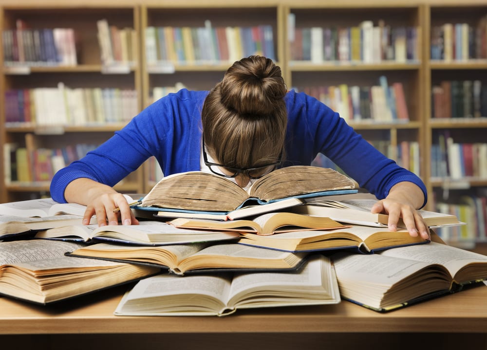 Girl studies for post-graduate degree with head in her books